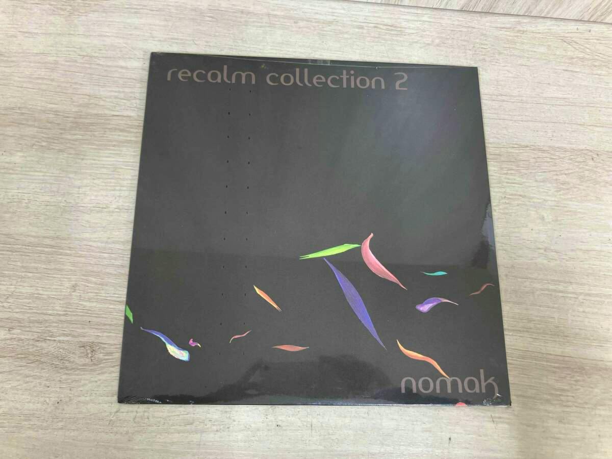 Front cover of the 12-inch vinyl record “Nomak Recalm Collection 2” showing a dark sleeve with colorful leaf-like shapes, photographed on a wooden surface.