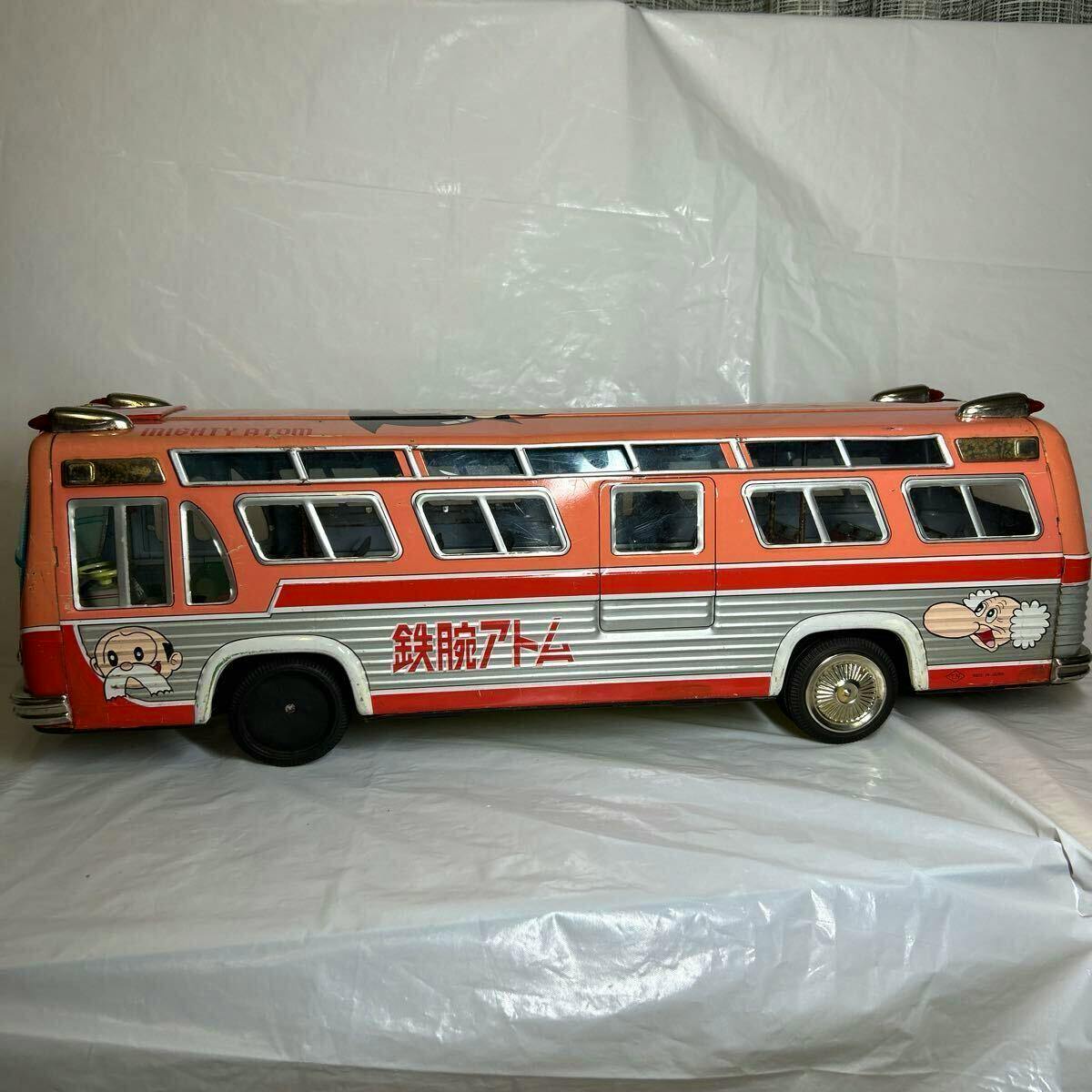 Side view of the Nomura Toy metal 'Tetsuwan Atom' GM bus toy showing an orange and silver body with character decals.
