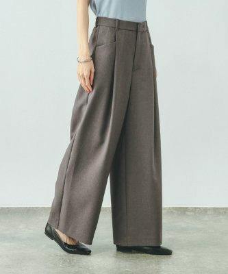A model wearing brown wide women's pants standing on a concrete floor, shown from mid-torso to feet.