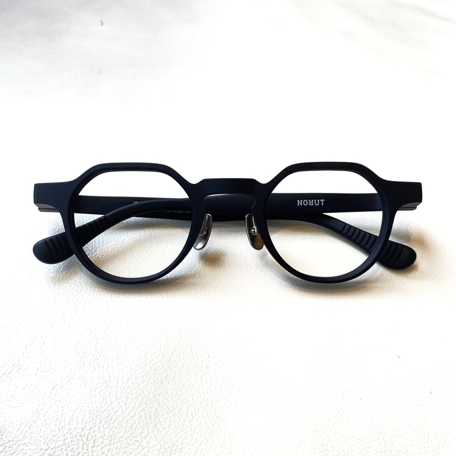 Front view of NORUT JOLY col.C-1 CLOSE YOUR EYES glasses showing a dark geometric round frame on a white surface.