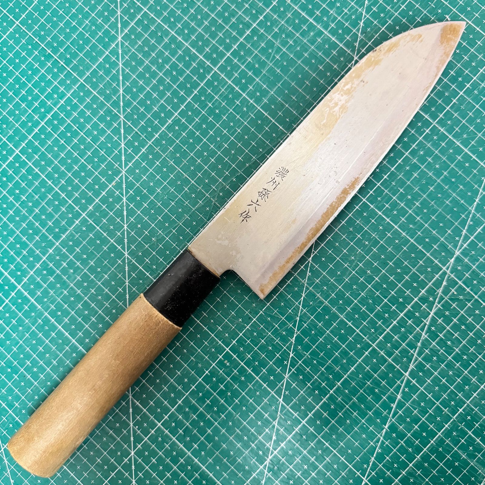 A Santoku chef knife (170mm) with a natural wooden handle and stamped stainless blade lying on a green cutting mat.