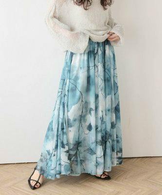 Model wearing a blue patterned sheer flare skirt standing against a white wall.