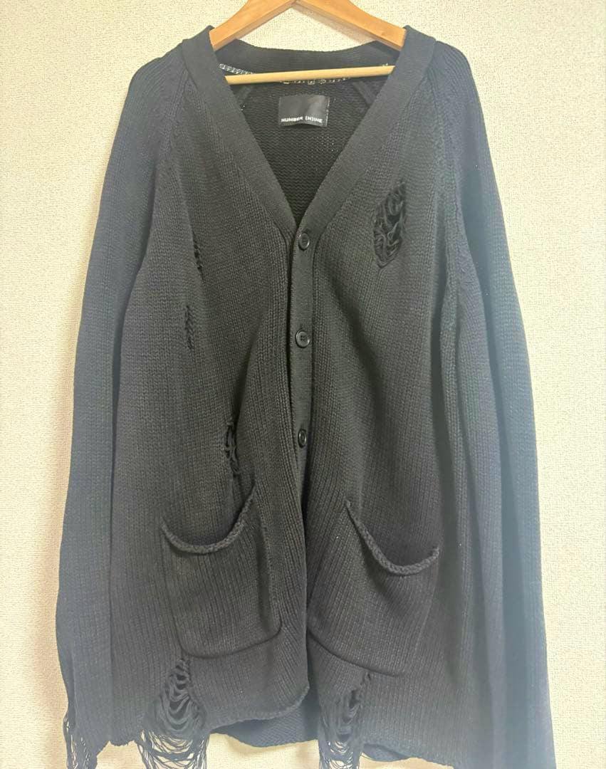 Front view of a black distressed NUMBER (N)INE cardigan hanging on a wooden hanger, showing buttons and front pockets.