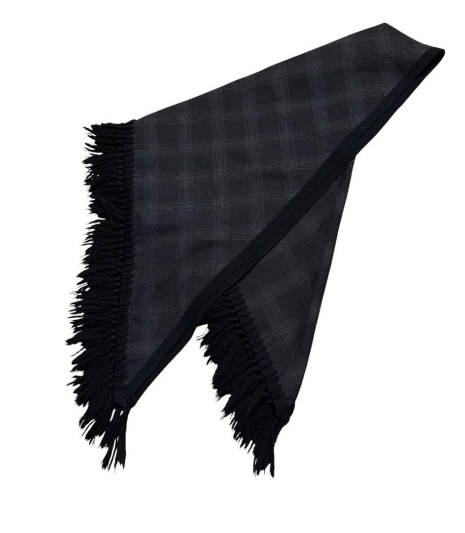 Dark check-patterned large fringed wool scarf folded and draped on a white background.