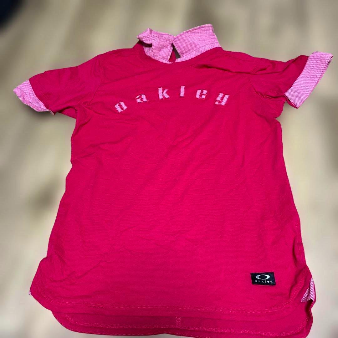 Front of a pink Oakley women's golf shirt laid flat showing "oakley" lettering across the chest and a small Oakley patch near the hem.