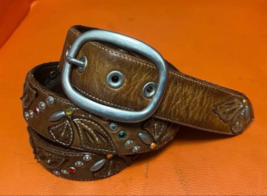 Brown cow leather belt with butterfly motifs, metal studs, and an oval metal buckle on an orange background.