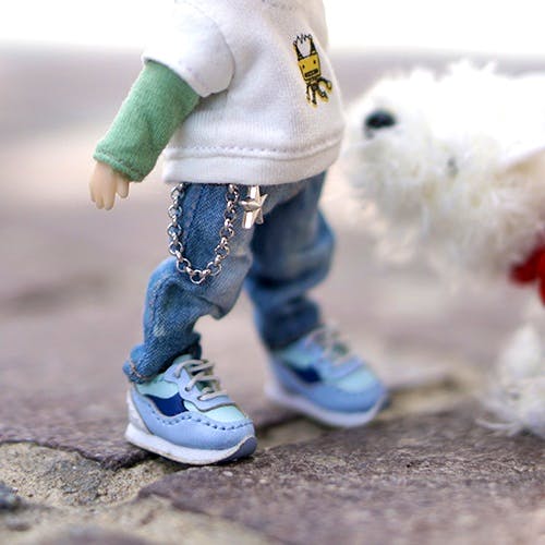 Obitsu11 doll wearing light blue sneakers and jeans standing on pavement with a small white dog in the background.