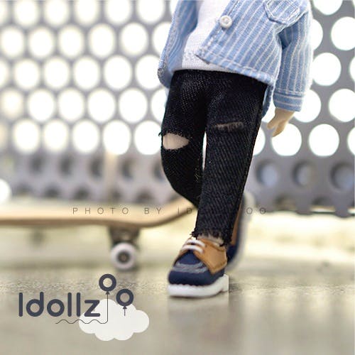 Close-up of an Obitsu11 doll wearing black ripped jeans and shoes, with a skateboard in the background.