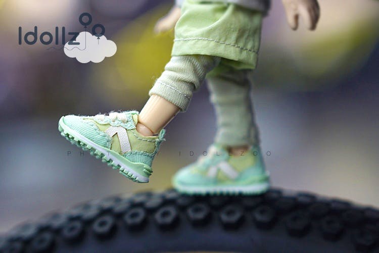 Mint-green Obitsu11 doll running shoe shown on a doll's foot balancing on a tire.