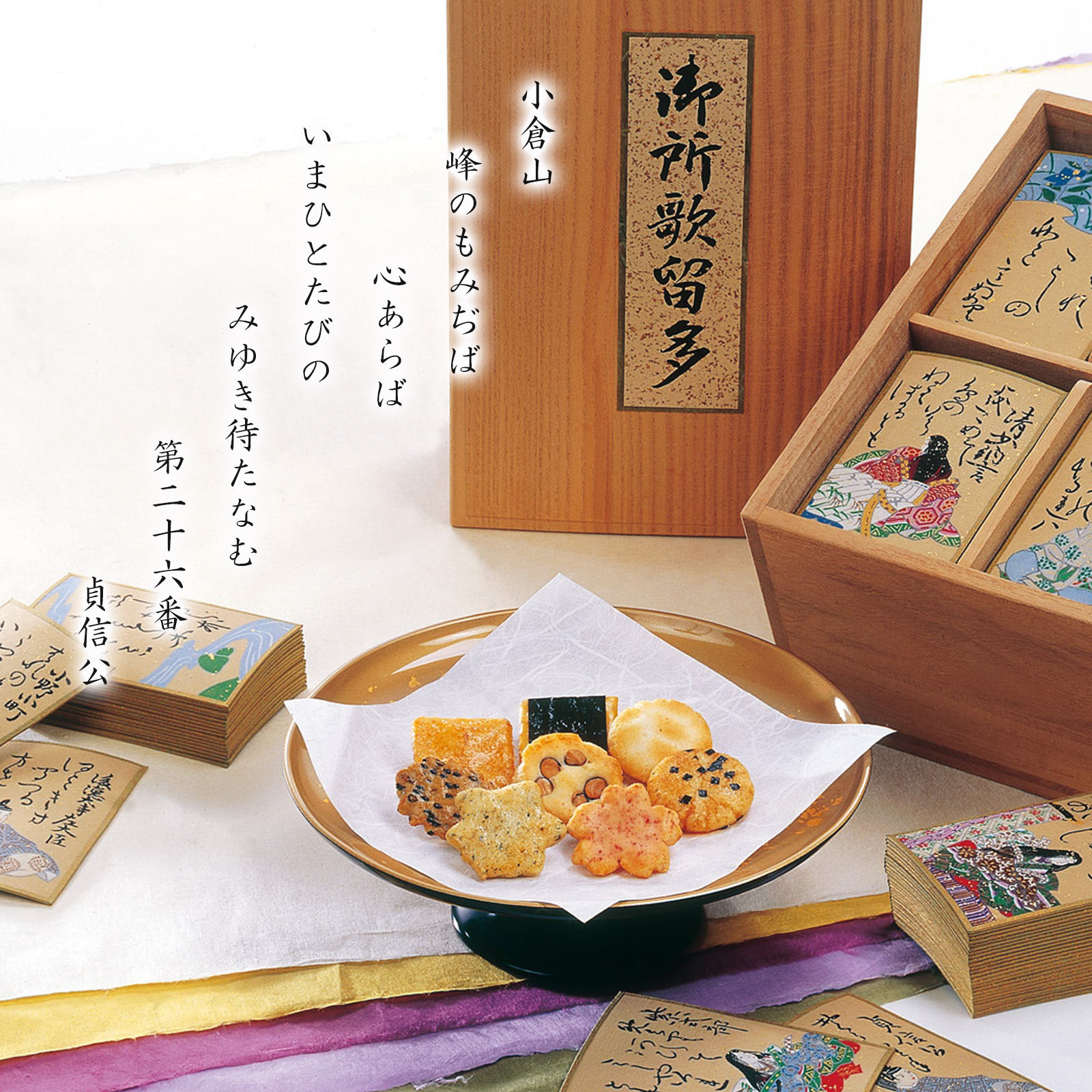 A wooden presentation box of assorted packaged rice crackers with several crackers displayed on a small plate and boxed packets around it.
