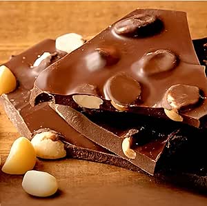 Close-up photo of broken chocolate bark pieces studded with macadamia nuts on a wooden surface.