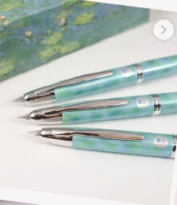 Three fountain pens with green-blue marbled barrels and chrome nib sections displayed on a white surface with a partial painting visible in the background.