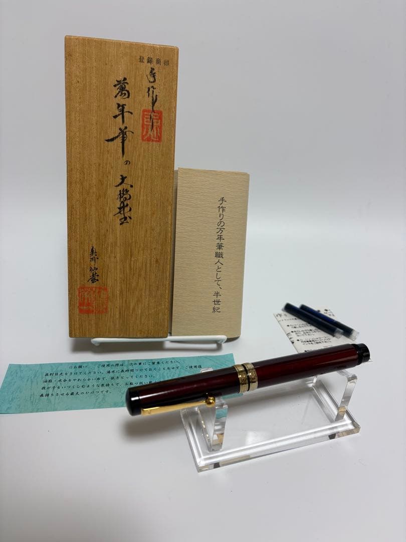 A fountain pen displayed on a clear stand with its wooden box and paperwork behind it.