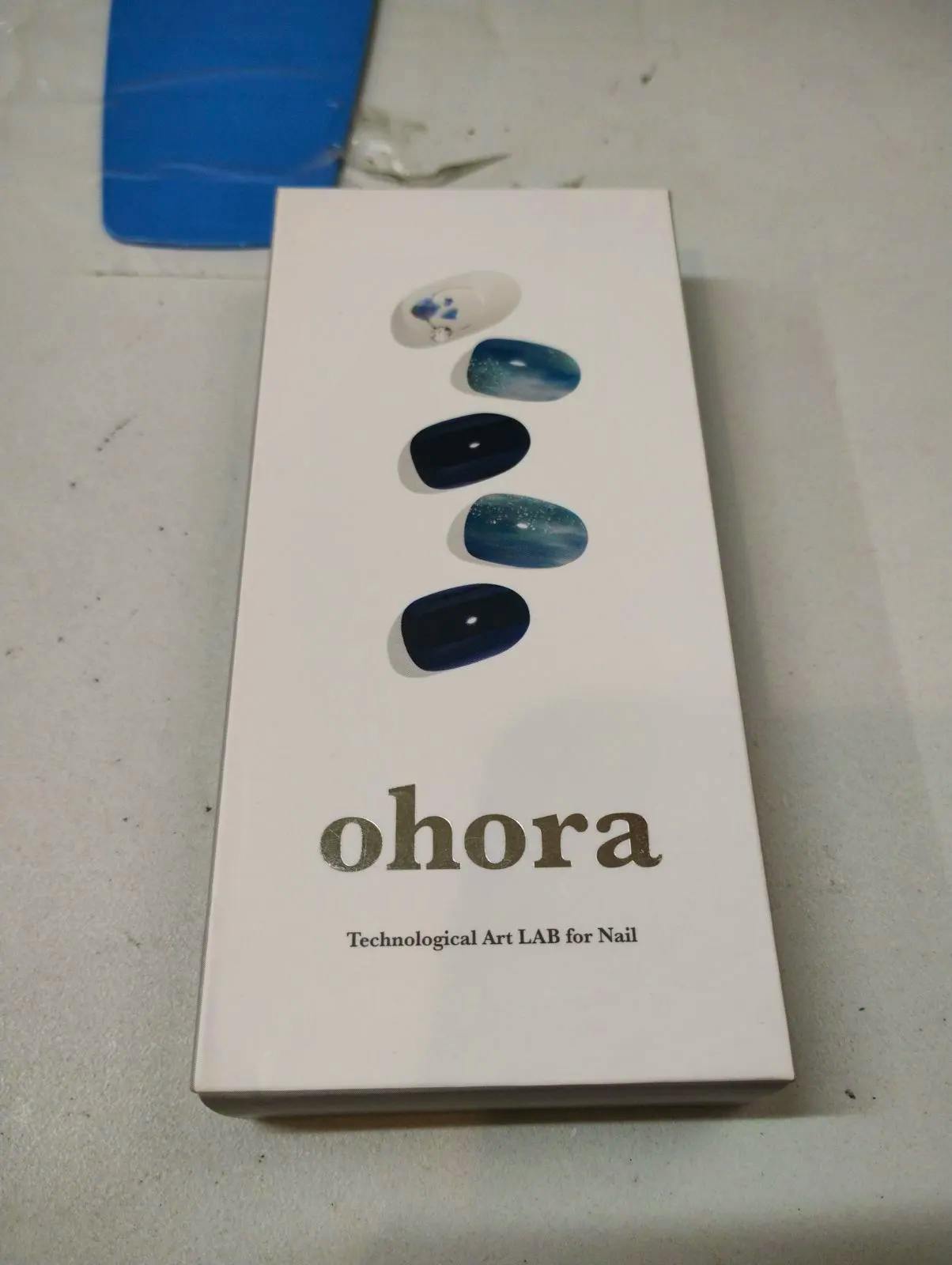 Photo of the ohora nail sticker box showing five blue-themed sample nail designs and the ohora logo.