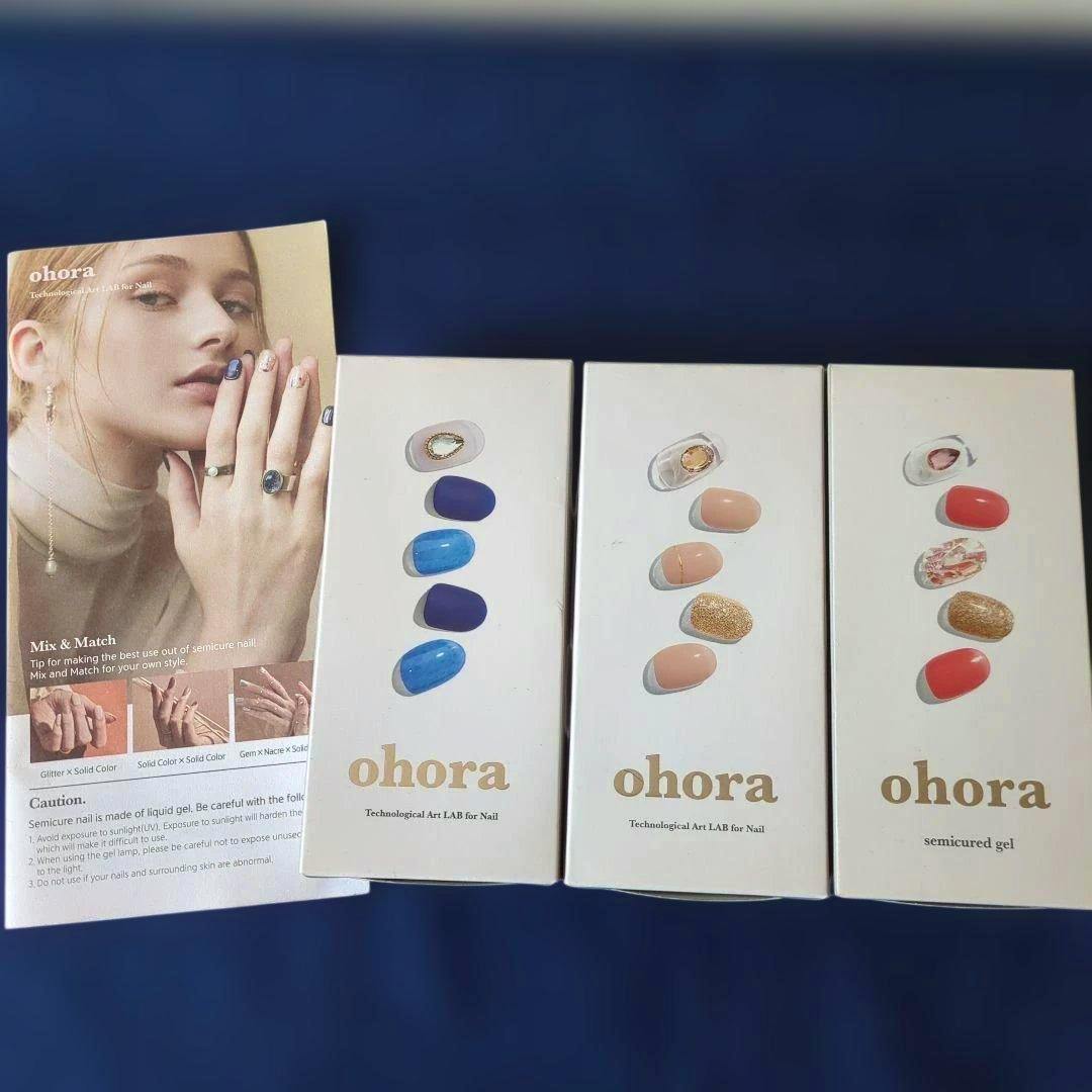 Three ohora semicur ed gel nail sticker boxes showing different nail designs and an instruction leaflet with a model's hand, arranged on a blue background.