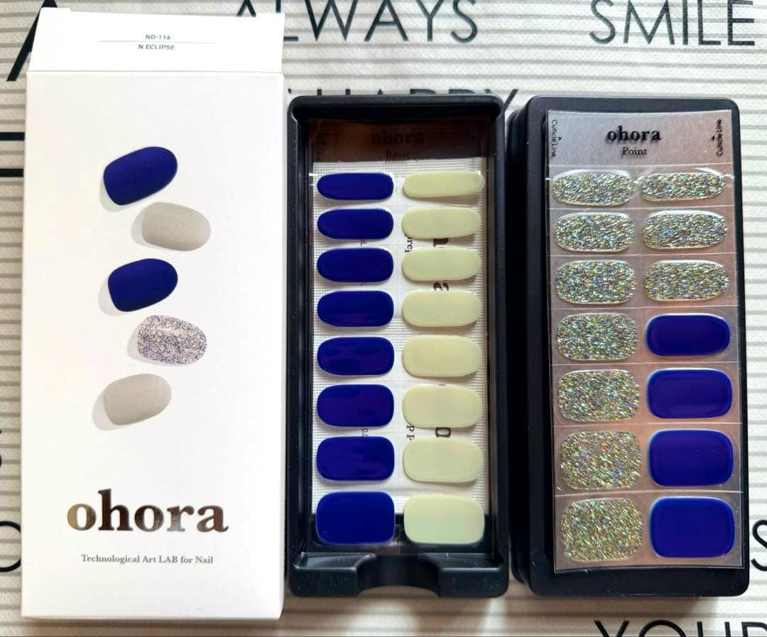 Photo of the ohora N Eclipse nail sticker set with its white box and two trays showing blue, pale, and silver glitter nail stickers.