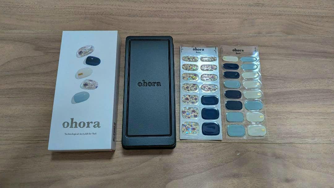 An ohora nail sticker set shown with its white product box, a black case, and three sheets of nail stickers laid on a wooden surface.