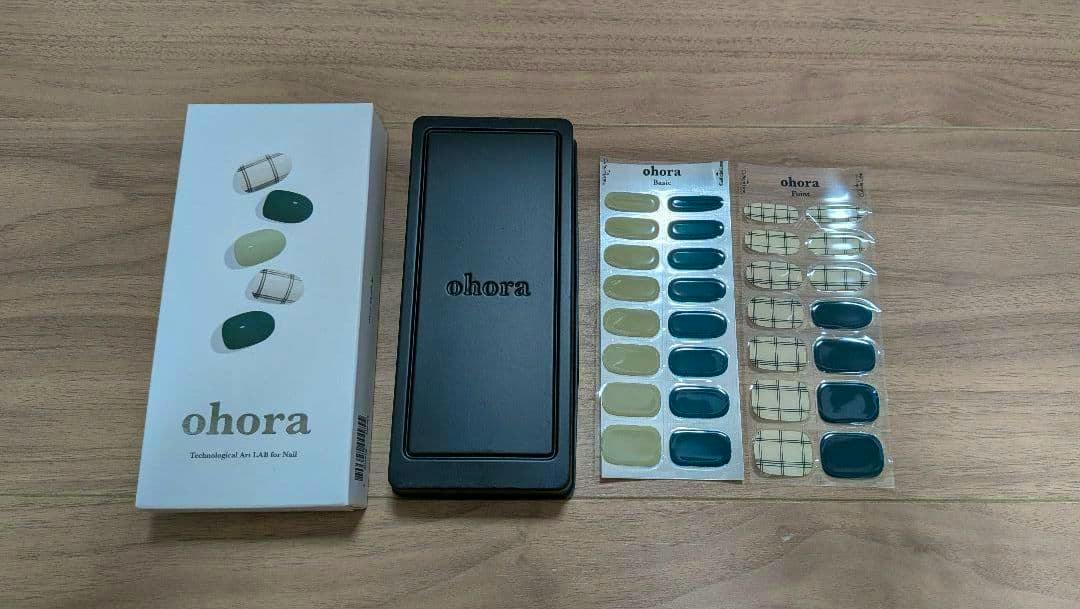 Two sheets of ohora nail sticker labels (green and check pattern) with the product box and a black case on a wooden surface.