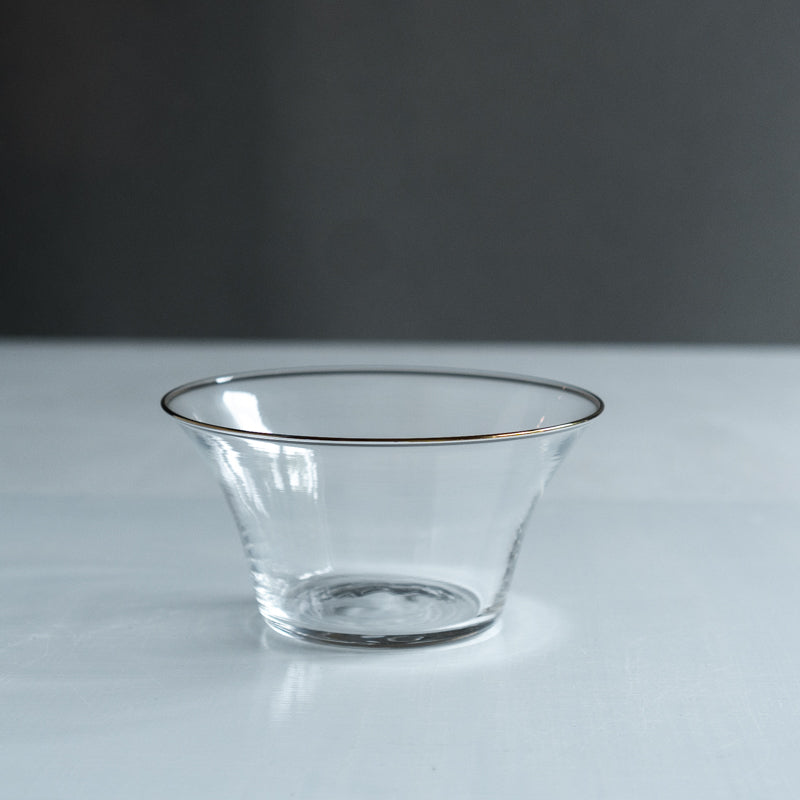 Clear glass bowl with flared sides and a thin dark rim on a light surface against a neutral background.