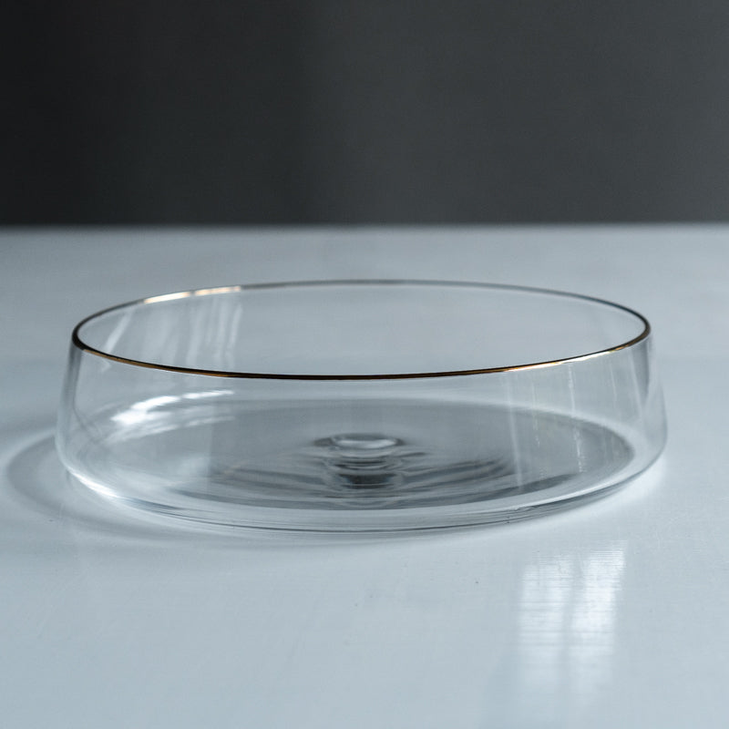 Clear shallow glass bowl with a thin gold-colored rim on a light surface.