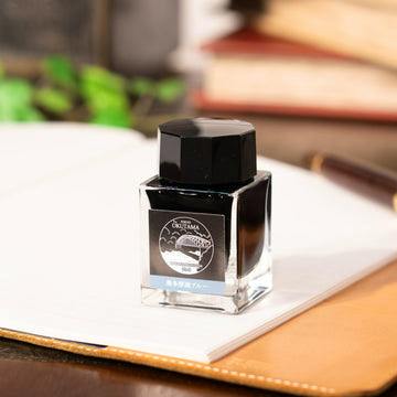 A 20ml Sailor “奥多摩湖ブルー” fountain pen ink bottle sitting on an open notebook.