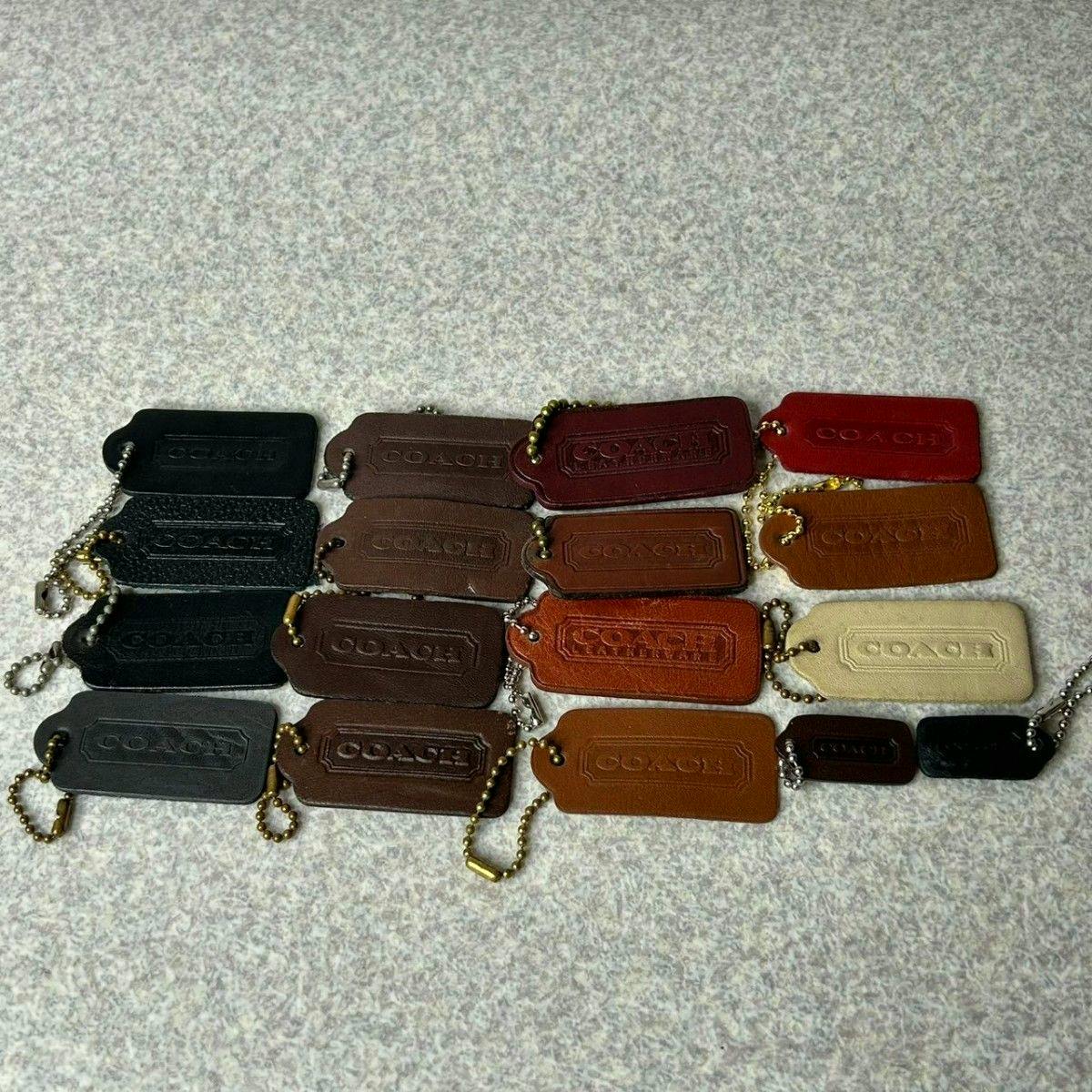 Multiple Old Coach leather key tags and bag charms in various colors arranged flat on a light fabric surface.