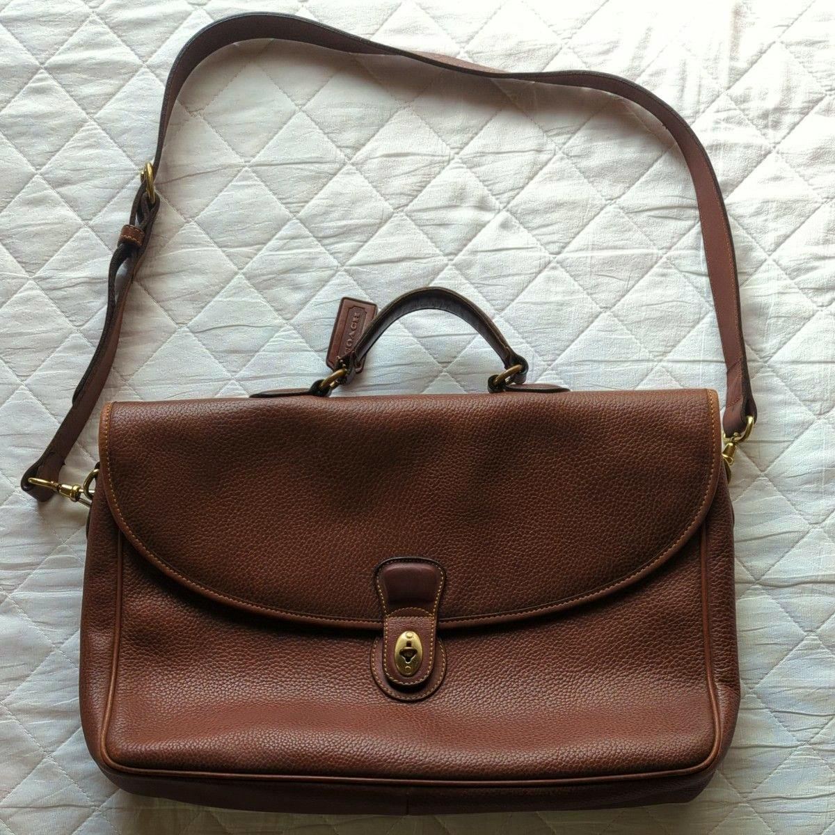 Brown leather briefcase-style shoulder bag with a top handle and a front turn-lock closure shown lying flat.