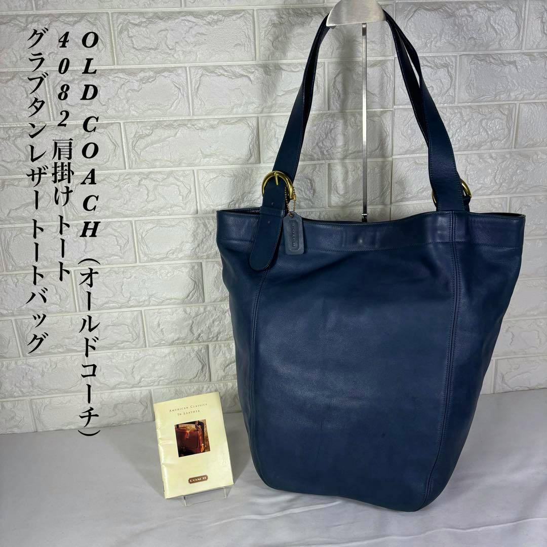 Dark blue OLD COACH 4082 tote bag with shoulder straps and a Coach hang tag displayed on a stand against a light tiled background.