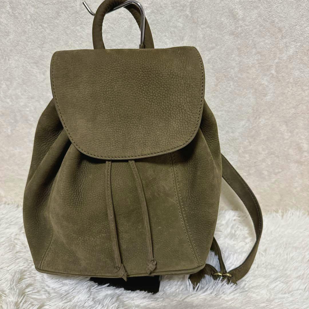 Front view of a khaki nubuck leather Coach backpack with flap closure and drawstring.