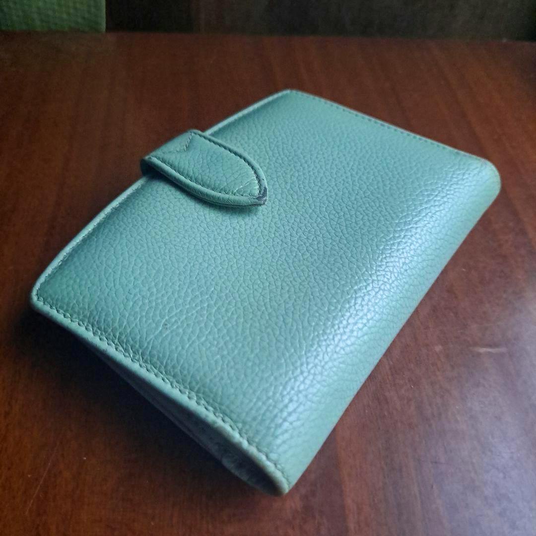 Pale green OLD COACH pebble-grain bi-fold wallet with a tab closure shown closed on a wooden surface.