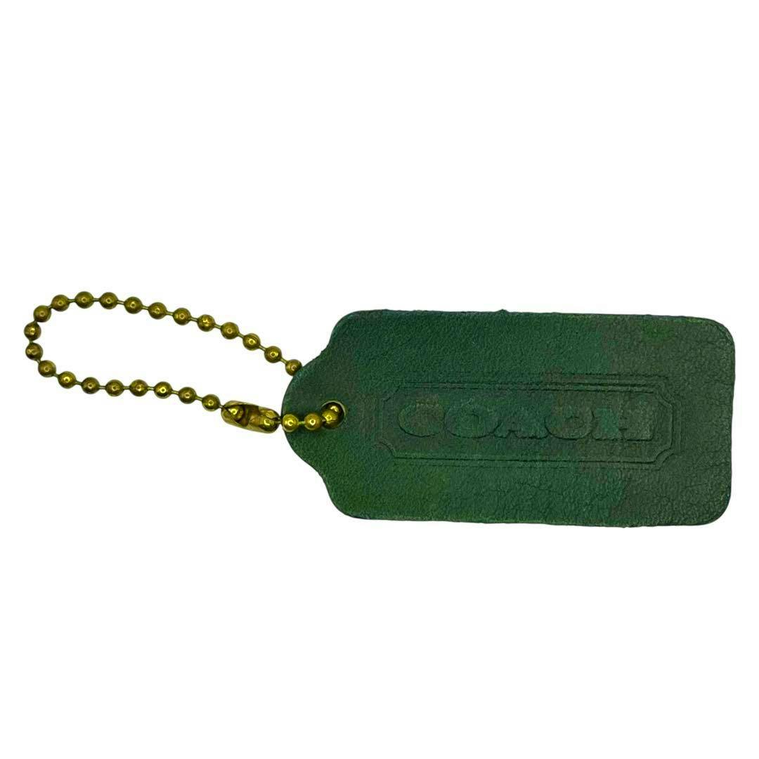 Green leather COACH hangtag charm embossed with the logo and attached to a brass ball chain on a white background.
