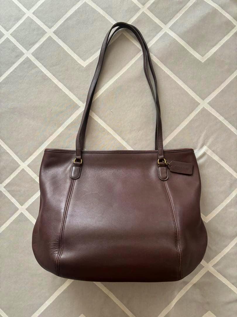 Dark brown leather shoulder bag laid flat showing the front, double shoulder straps, and a hanging leather tag.