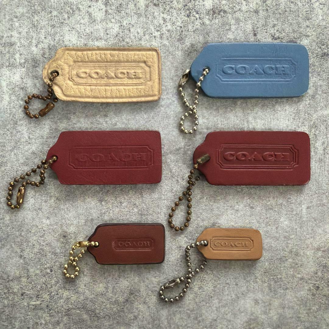 Several leather COACH hangtag keychain charms in different colors arranged on a gray surface.