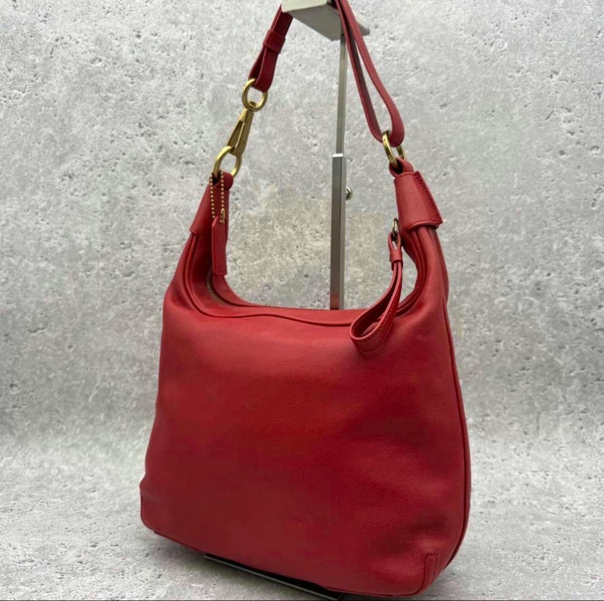 Red leather Old Coach hobo shoulder bag hanging on a display stand, showing the strap and gold hardware.