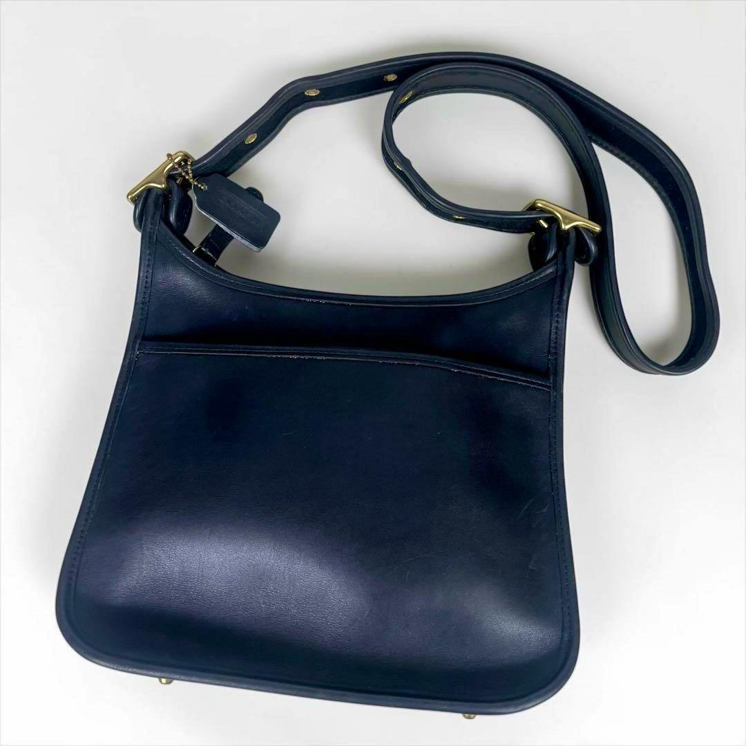 Old Coach black leather shoulder bag lying flat showing the front, strap, and brass hardware.