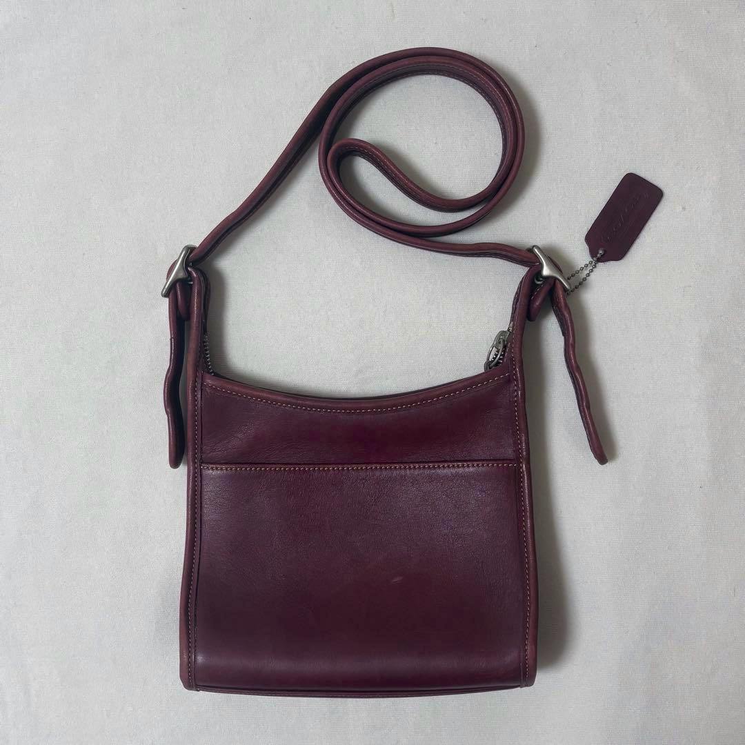 Front view of an Old Coach bordeaux leather shoulder bag with shoulder strap and hang tag on a light background.