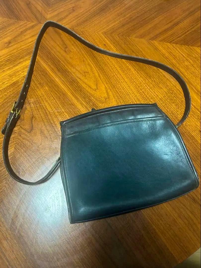 Navy cow leather Old Coach shoulder bag with a brown adjustable strap lying on a wooden table.