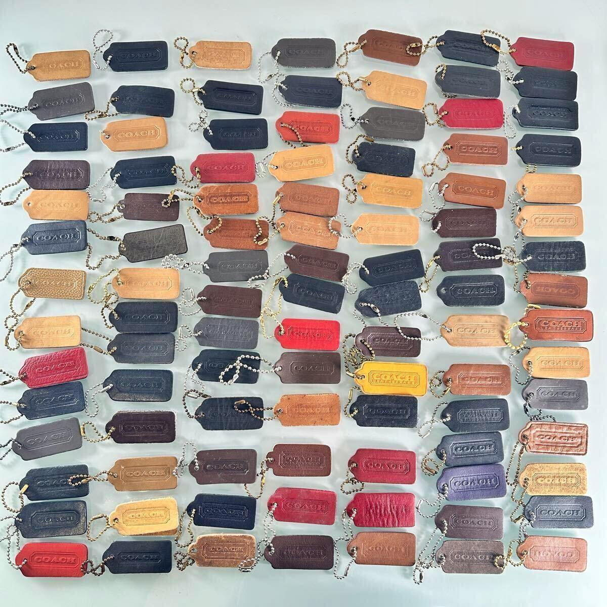 Many COACH leather tag keychain charms in various colors arranged in rows on a light background.