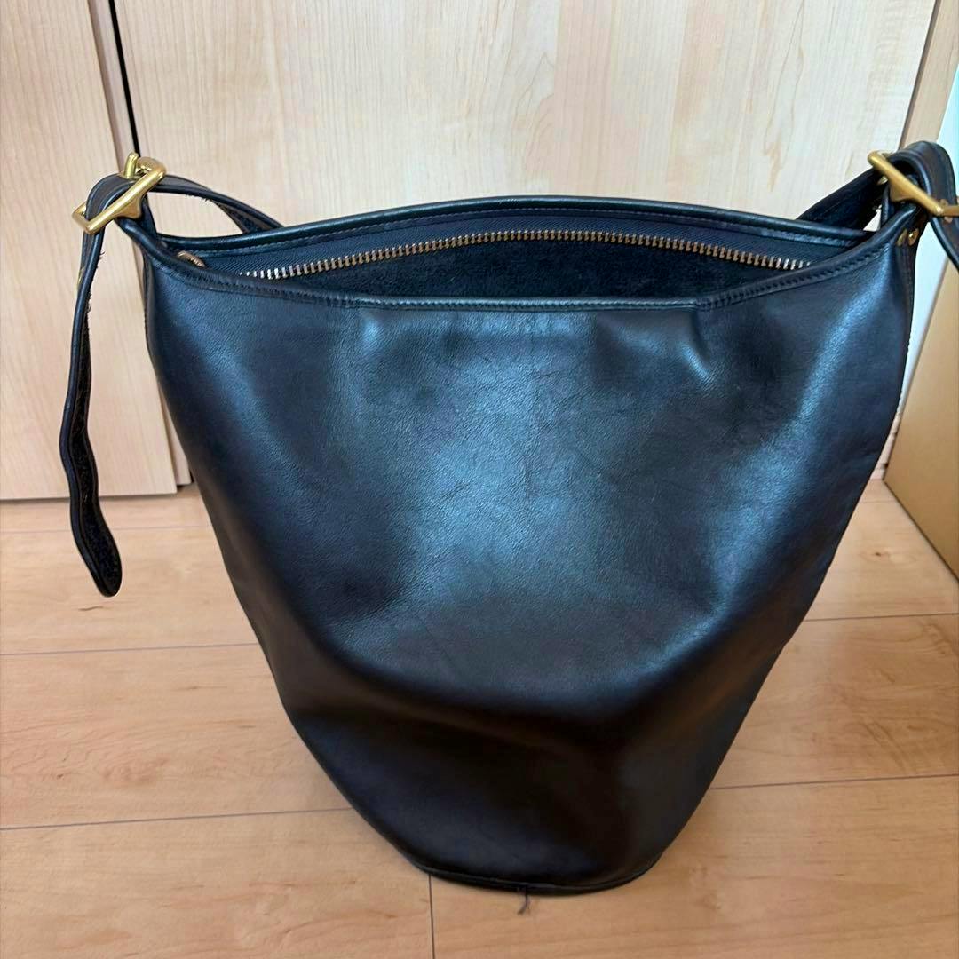 Black leather bucket shoulder bag with a top zipper and adjustable strap, shown from the front.