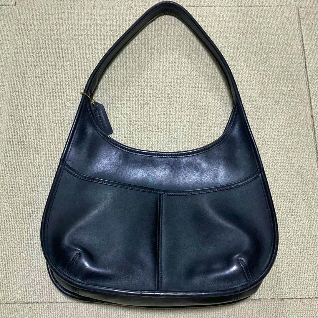 Old Coach black one-handle cow leather hobo shoulder bag lying flat on a light carpeted background.
