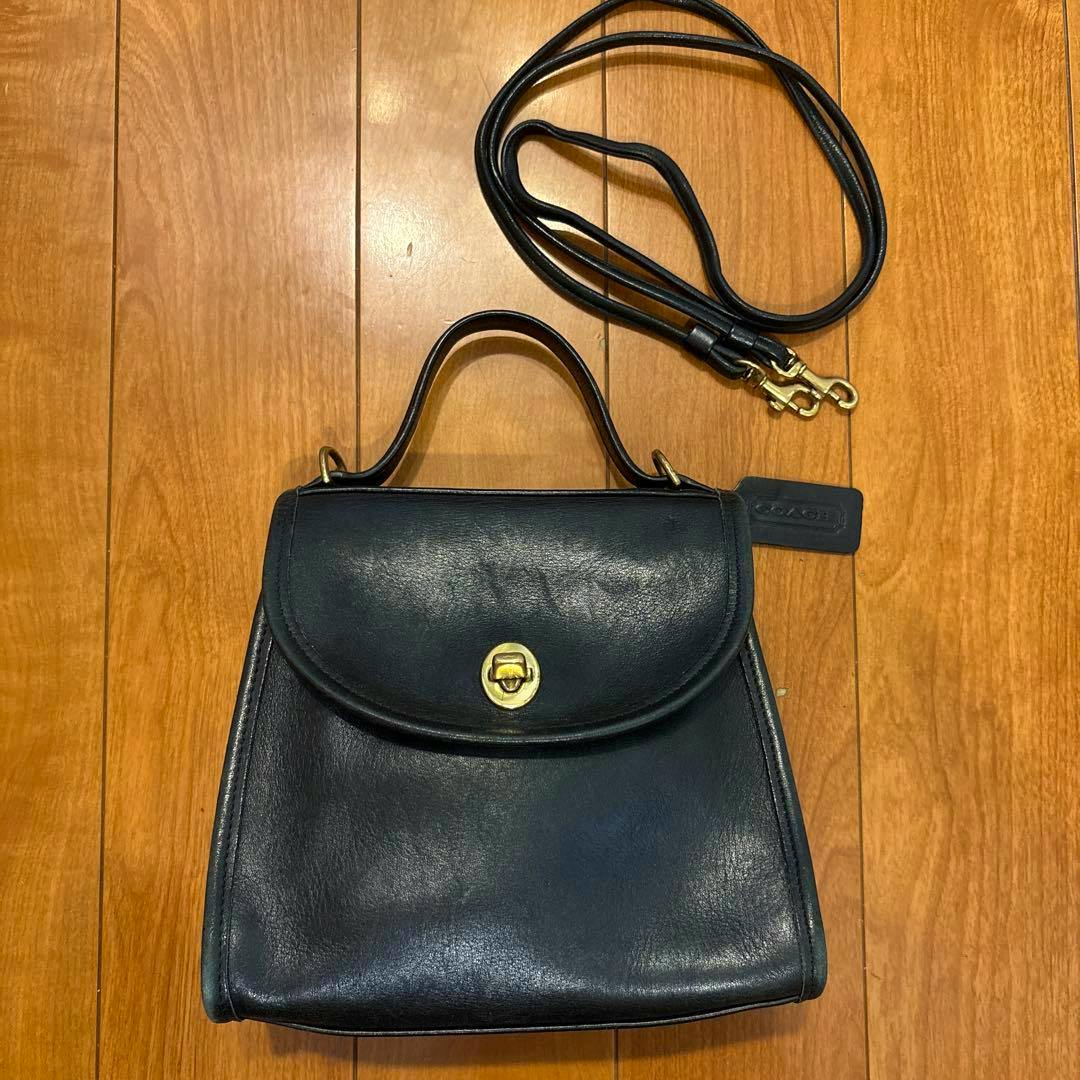 Black Coach Regina leather shoulder bag with top handle and detached shoulder strap photographed on a wooden floor.