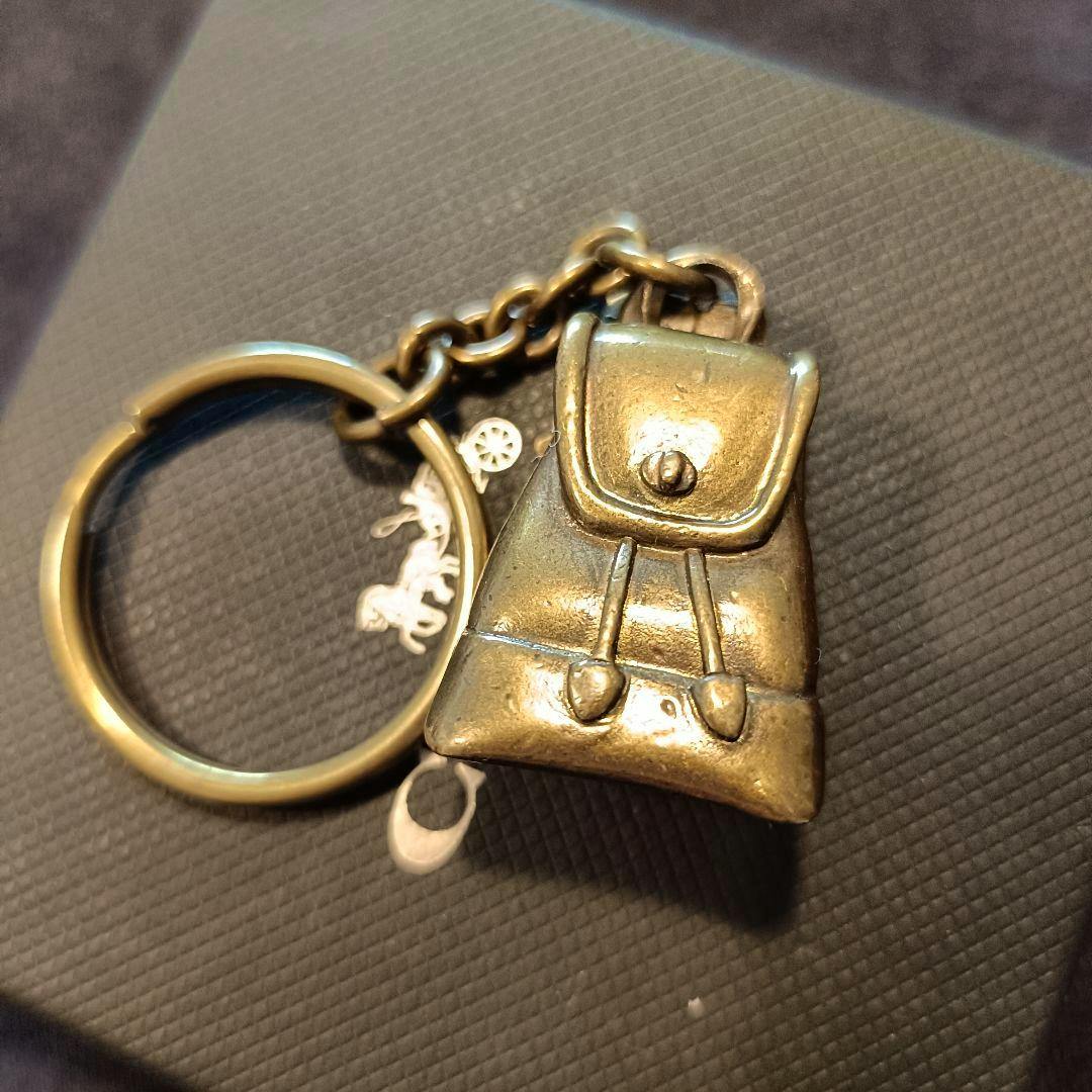 A zinc-alloy backpack-shaped bag charm keychain with a turn-lock flap attached to a key ring.