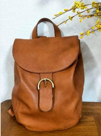 Front view of a brown cow leather vintage Coach backpack on a wooden surface.
