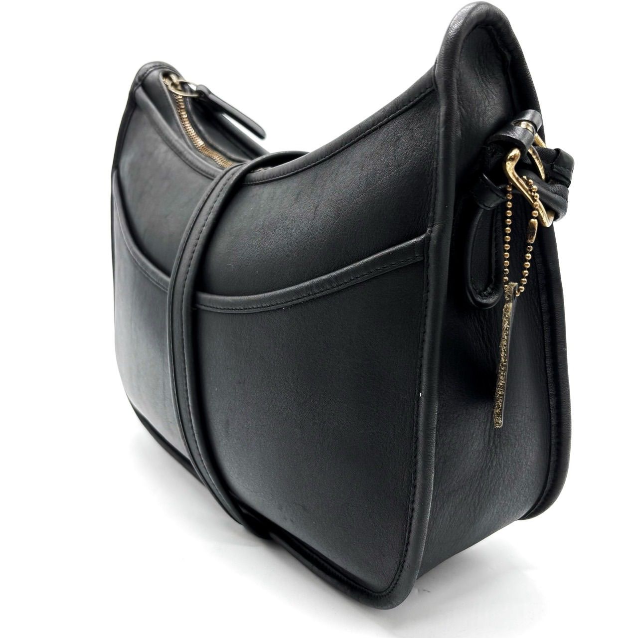 Old Coach black leather shoulder pochette bag shown at a three-quarter side view with visible zipper and metal pull.