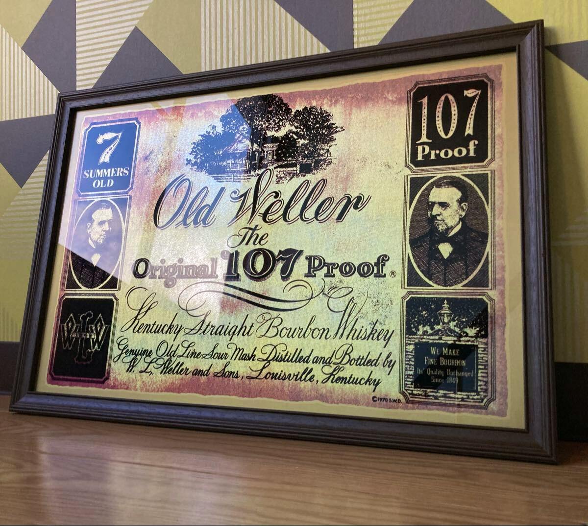 Framed wooden vintage-style wall sign reading "Old Weller The Original 107 Proof" leaning against a patterned wall.