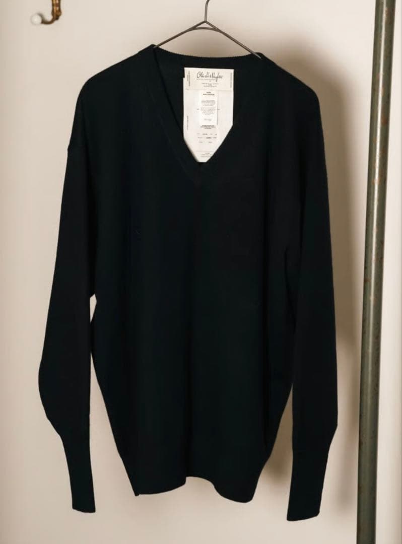 A dark Olde H & Daughter cashmere V-neck sweater hanging on a hanger with the label visible.