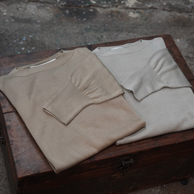 Two folded silk crewneck sweaters laid on a wooden chest.
