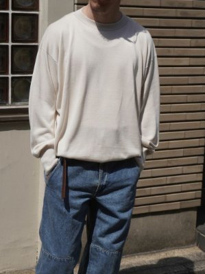 Model wearing a milk-colored silk crew neck sweater shown from the thighs up with hands in pockets.