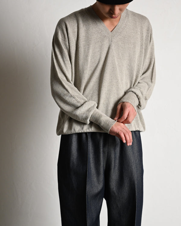 A person wearing a light grey V-neck silk sweater, shown from mid-thigh up while adjusting the sleeve.