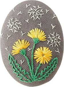 Oval embroidered brooch with yellow French-style thread flowers on a gray background.